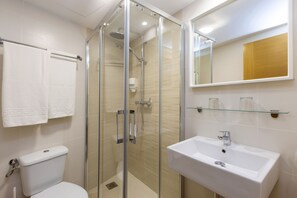 Un baño moderno con ducha de vidrio, un lavabo blanco y un inodoro.