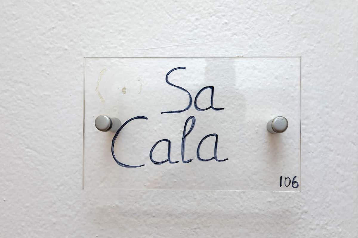 A clear glass sign with the text "Sa Cala" and the number "106" on a white wall.