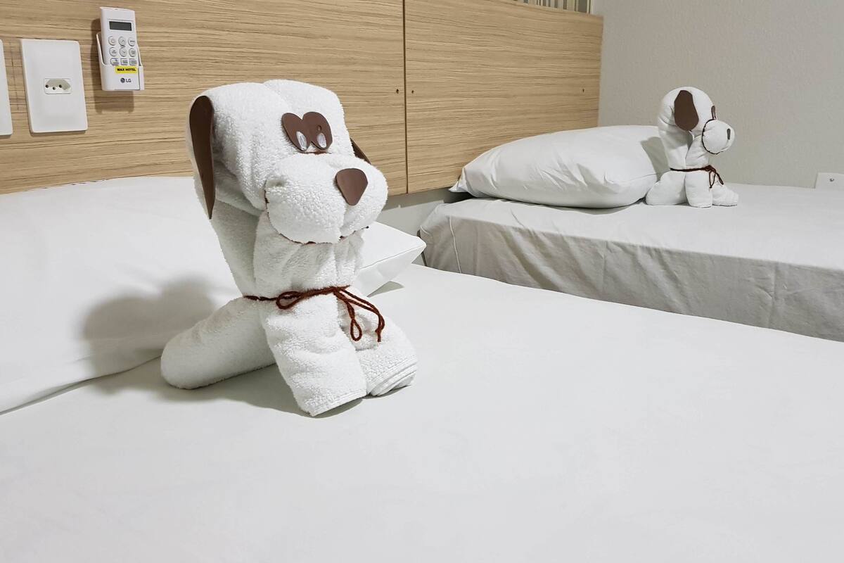 Hotellihuone, jossa on kaksi sänkyä, ja jokaisessa sängyssä on pehmeä, koiran muotoinen koristetyyny.