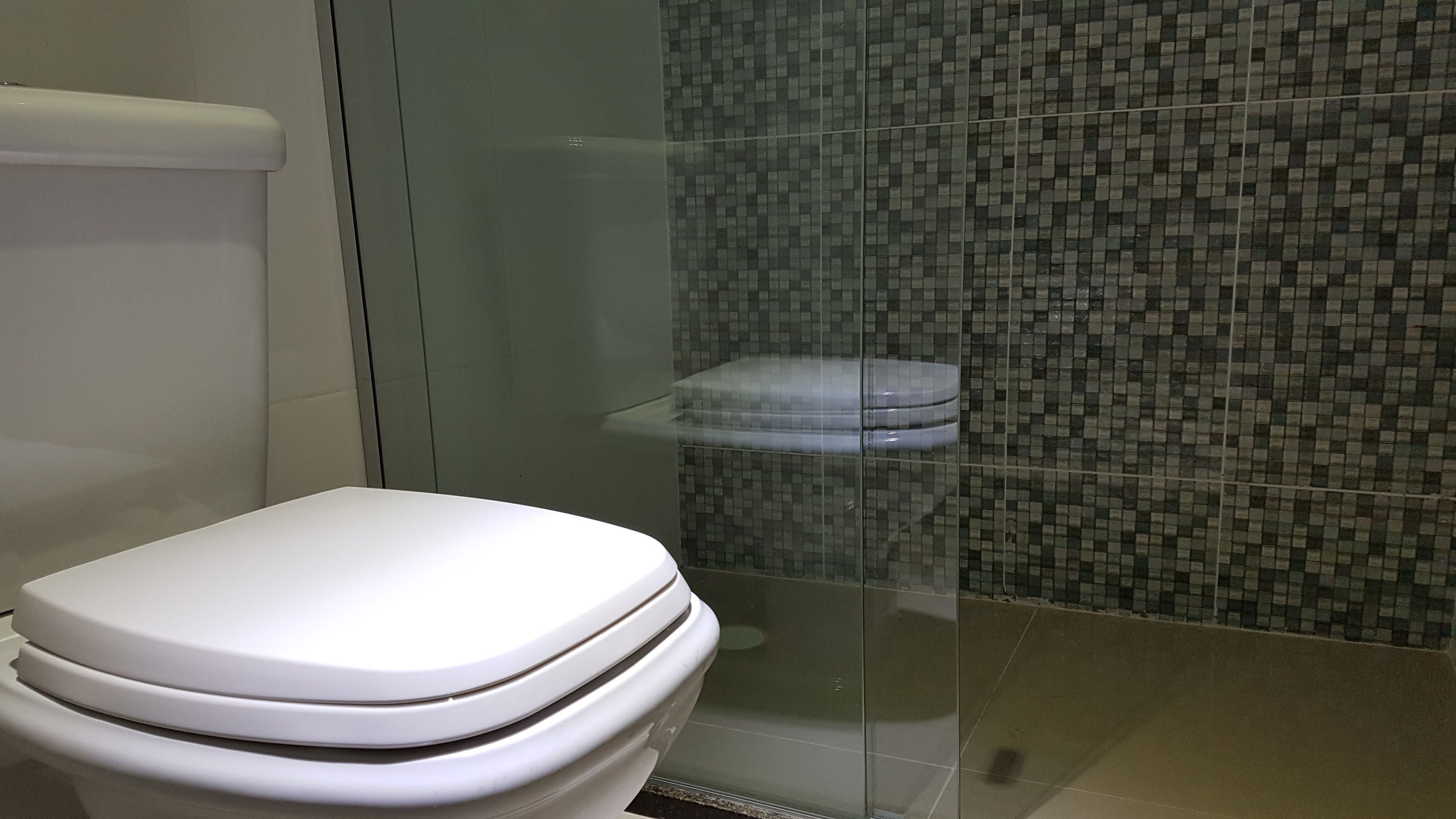 A modern bathroom with a white toilet, a glass shower enclosure, and a tiled wall.