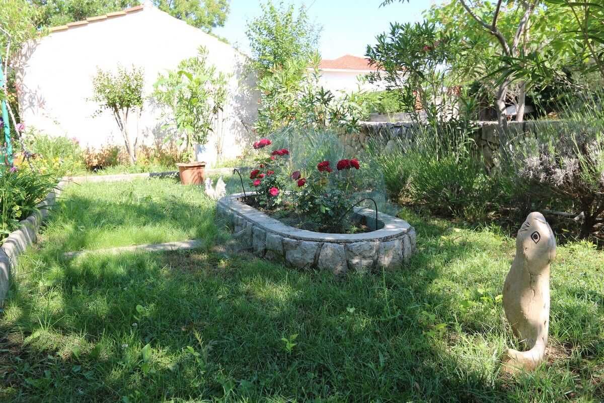 Un jardín con una jardinera de piedra circular, una estatua y un edificio al fondo.