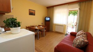 Ett kompakt bostadsutrymme med ett litet kök, en matplats och en soffa med ett mönstrat kuddöverdrag.