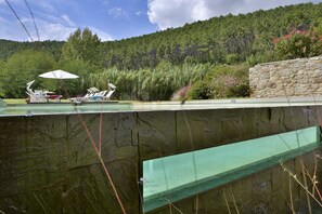 A swimming pool with a stone wall, surrounded by greenery and a stone building.