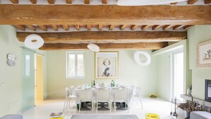 A dining area with a round table set for four, surrounded by white chairs. There is a yellow vase on the table, and a framed picture hangs above it. - Villa for 10 People with WiFi, Private Pool, Garden, A/C, near Lucca (Vorno)