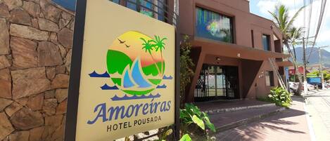 A sign for Amoreiras Hotel Pousada with a logo featuring a sailboat, palm trees, and a sunset.