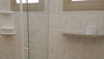 Un baño con ducha de vidrio, inodoro y repisa con artículos de aseo.