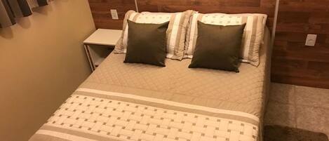 A neatly made bed with a quilted headboard, two pillows, and a bedside table.