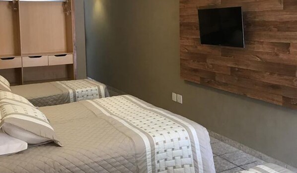 A bedroom with two beds, a wooden wall panel, and a mounted TV.