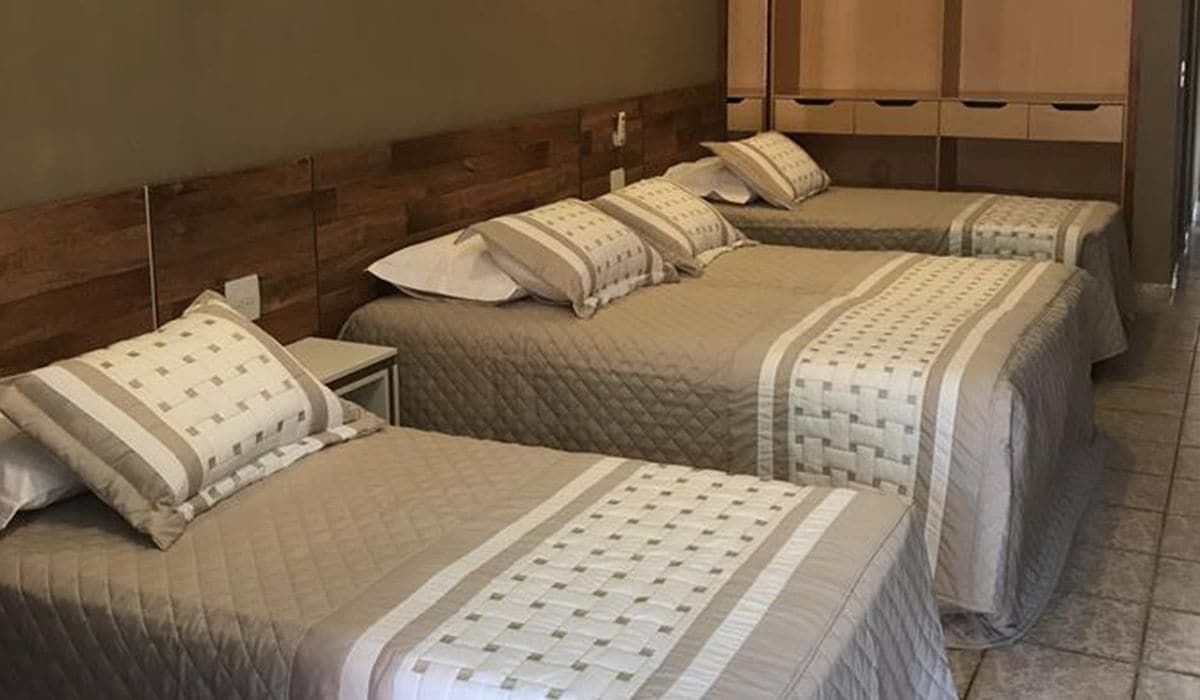 A hotel room with three beds arranged in a row, each with a wooden headboard and matching bedding.