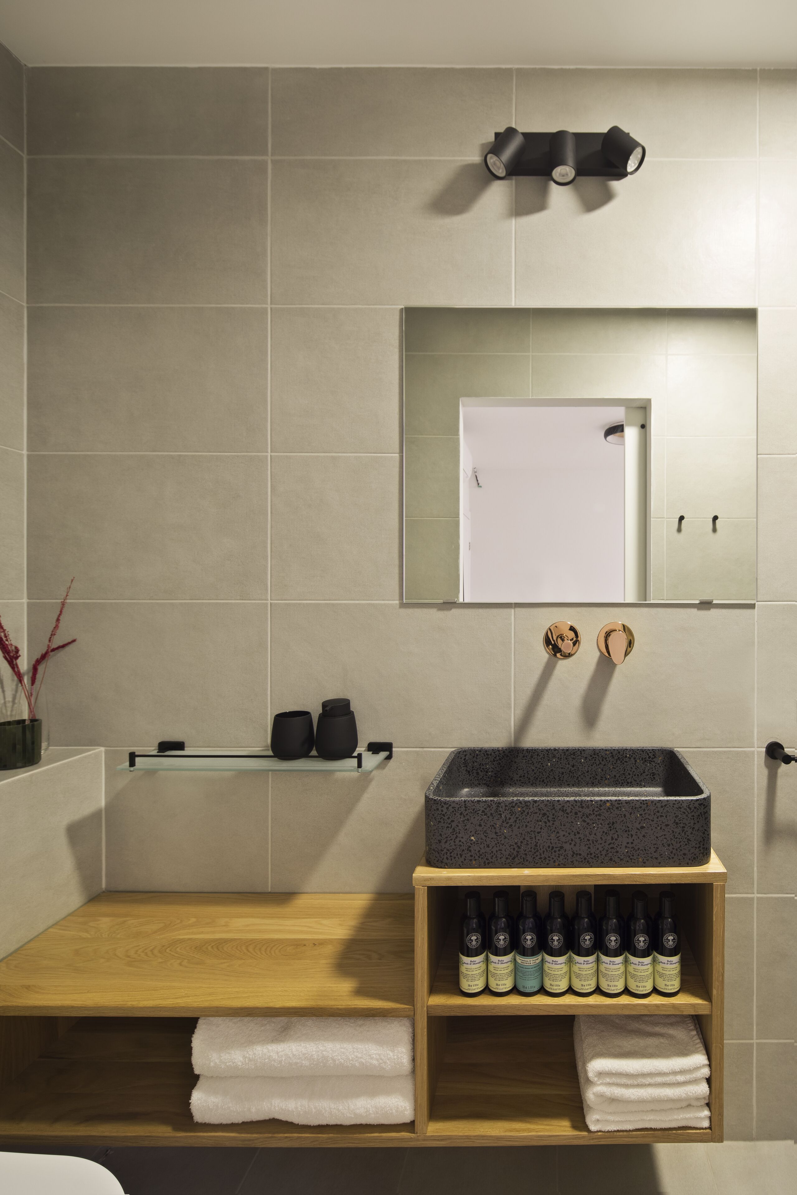 Un bagno moderno con un mobile bagno in legno, uno specchio grande e uno scaffale con articoli da toilette.