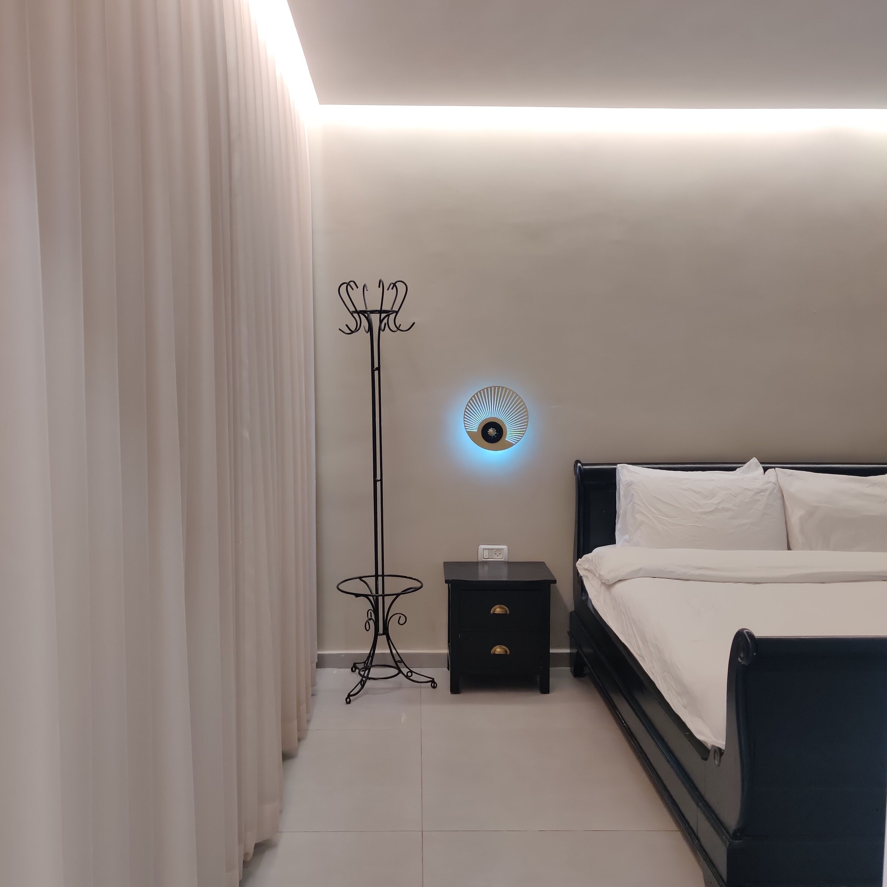 A bedroom with a bed, a nightstand, a floor lamp, and a wall-mounted light fixture.