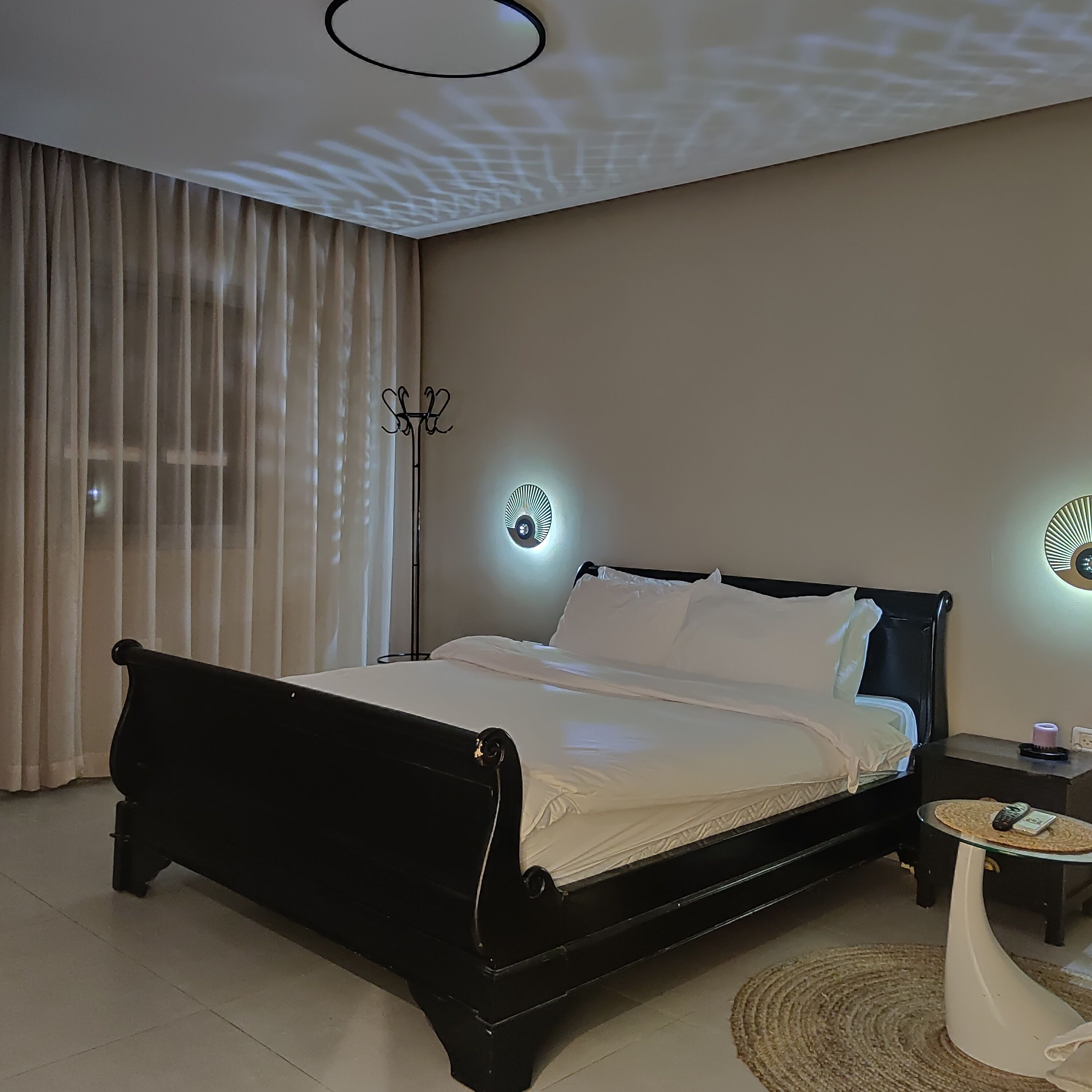 A modern bedroom with a black bed frame, a round ceiling light, and a bedside table with a lamp.