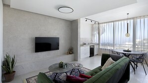 Uma sala de estar moderna com televisão de tela plana, um sofá verde, uma mesa de centro e uma área de jantar com mesa redonda e cadeiras.