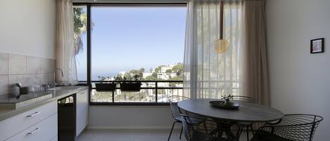 A modern kitchen with a dining area, large windows, and a view of the city.
