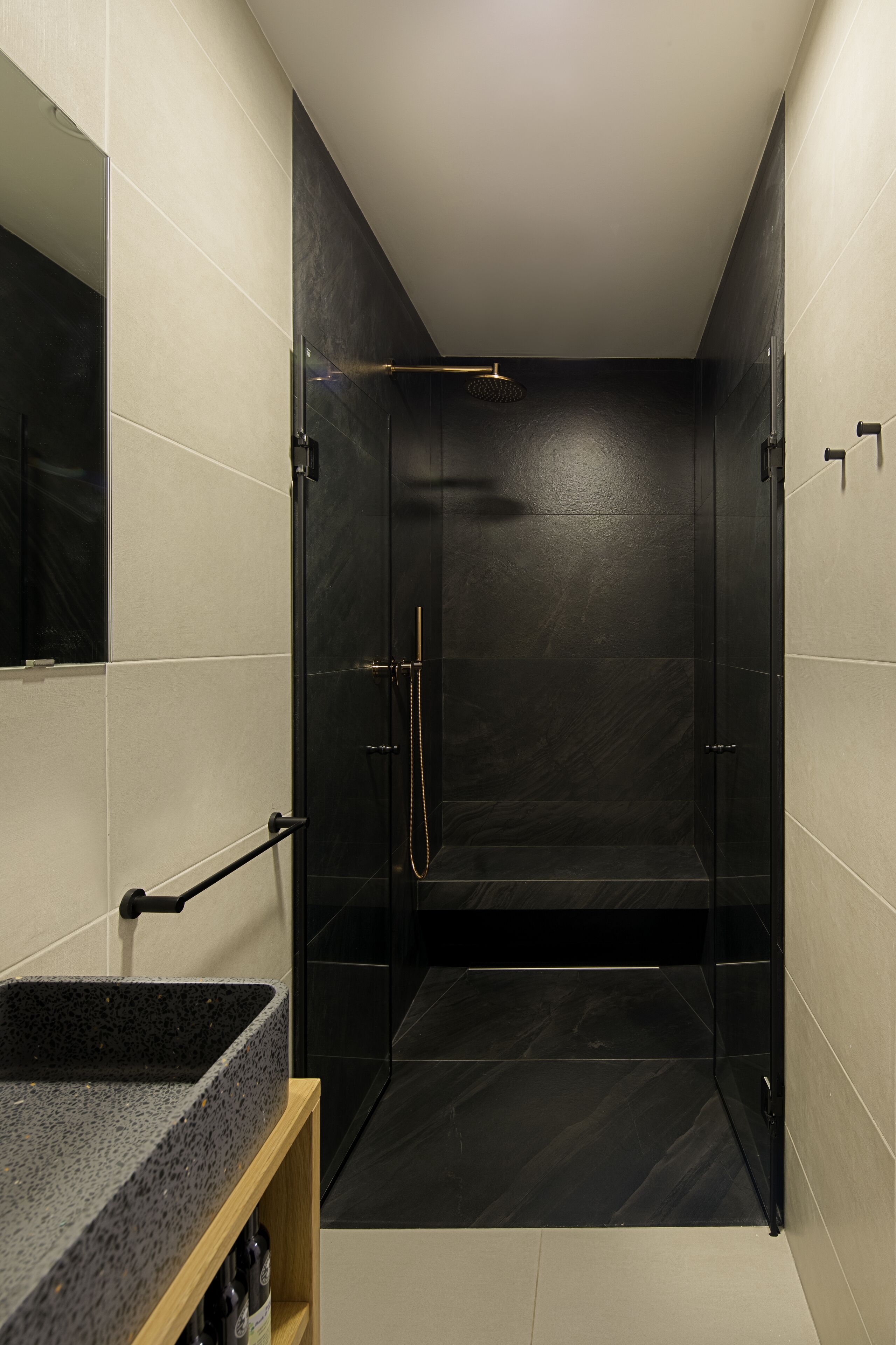 Un baño moderno con ducha envuelta en vidrio, tocador de madera con lavamanos y espejo.