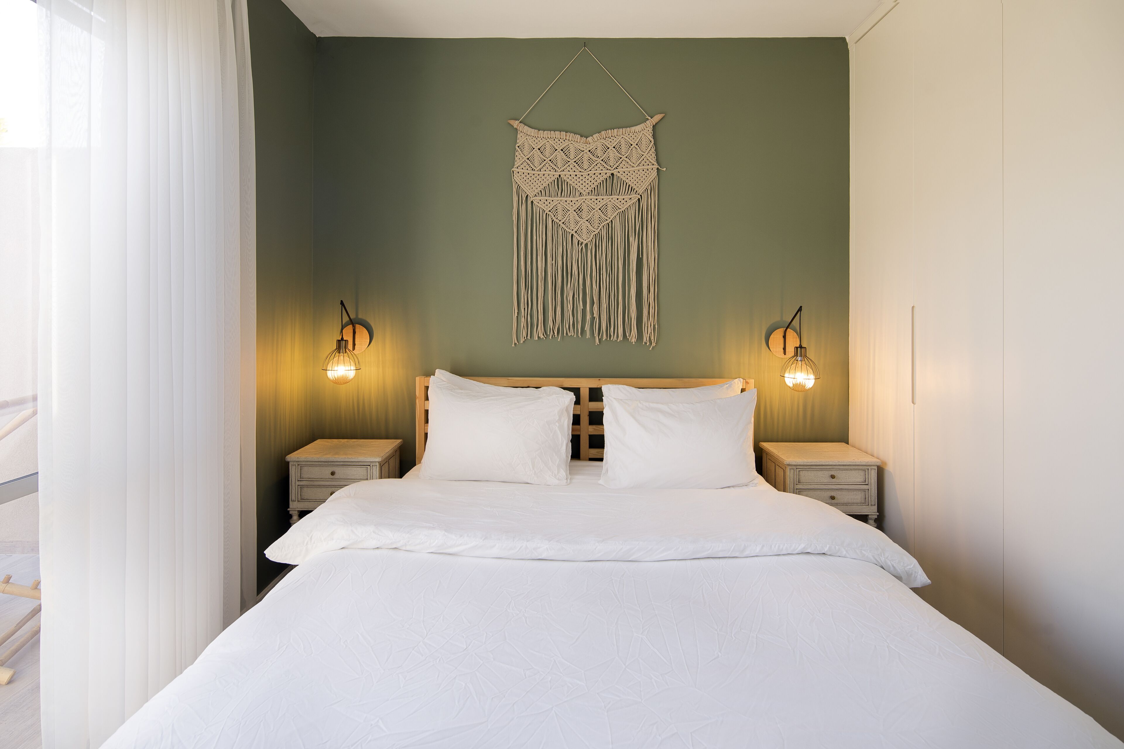 A neatly made bed with white linens, two bedside tables with lamps, and a wall hanging above the bed.