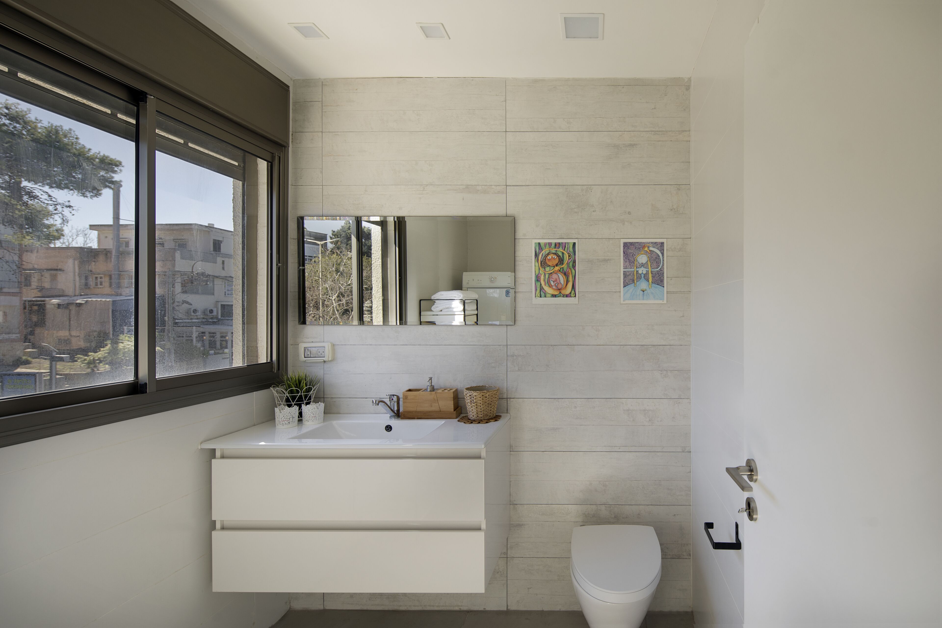 A modern bathroom with a white vanity, a toilet, and a large window.