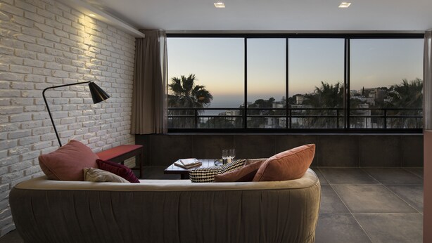 Uma sala de estar moderna com uma janela grande, um sofá, uma mesa com copos e um abajur.