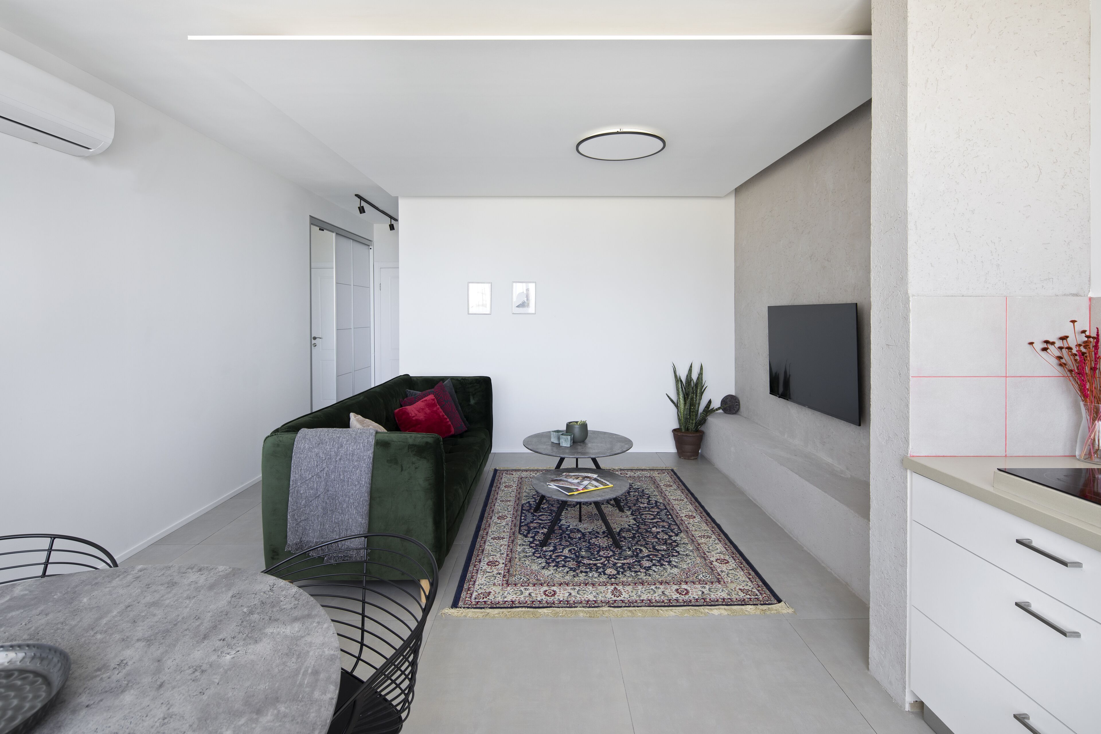 A modern, minimalist living space with a green sofa, a round coffee table, a small rug, and a flat-screen TV mounted on the wall.