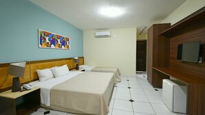 Une chambre d’hôtel avec un grand lit, des tables de chevet, un téléviseur, un appareil de climatisation et un tableau coloré accroché au mur.