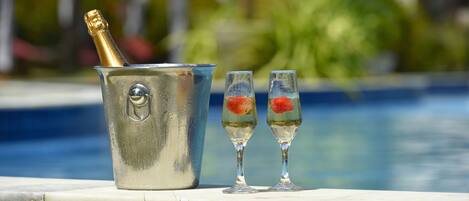 A champagne bucket and two glasses with fruit floats by a pool.