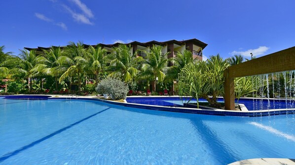 Una piscina con agua azul cristalina, rodeada de palmeras y un edificio con balcones.