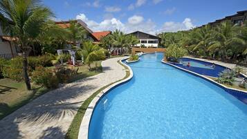 A large, clear swimming pool with a curved edge, surrounded by palm trees and a paved walkway.