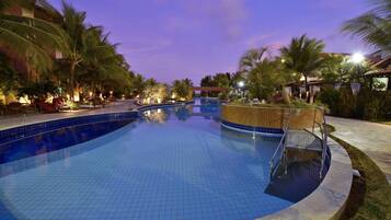 Una piscina con bordes de azulejos, rodeada de palmeras y sillas de descanso, bajo un cielo crepuscular.