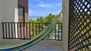 Un hamac sur un balcon avec vue sur l’océan et les palmiers.
