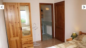 A bedroom with a wooden wardrobe, a bed with a quilt, a bedside lamp, and a view of a balcony through an open door.