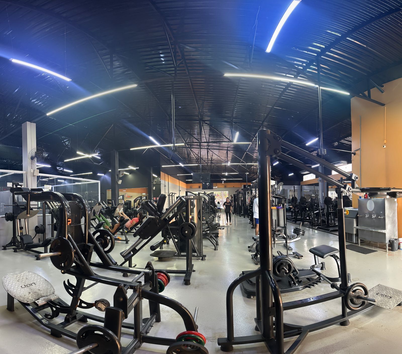 Un gimnasio con diversos equipos de ejercicio, techo alto y un espacio amplio.