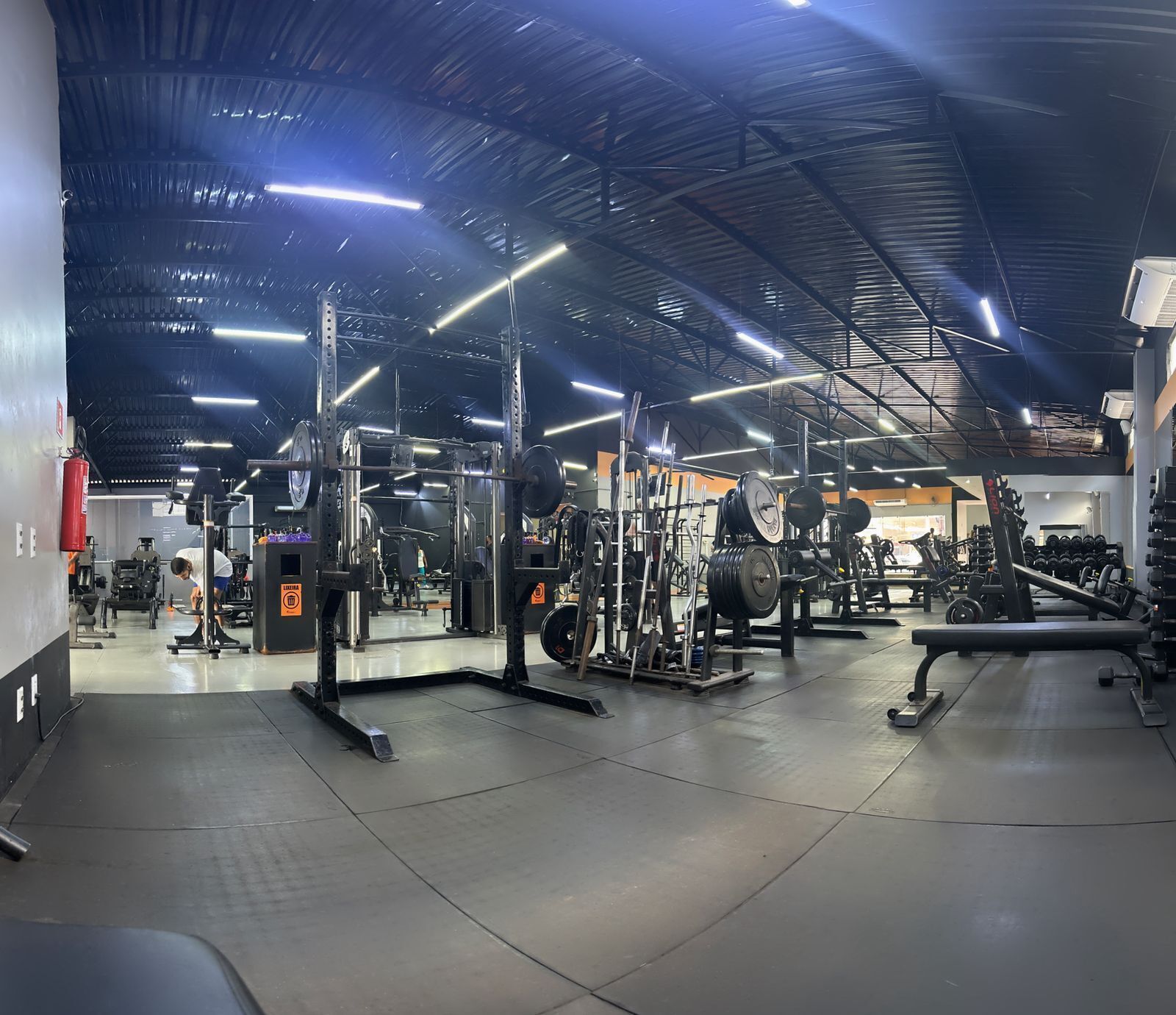Un gimnasio con equipo de levantamiento de pesas, una banca y un espejo grande.