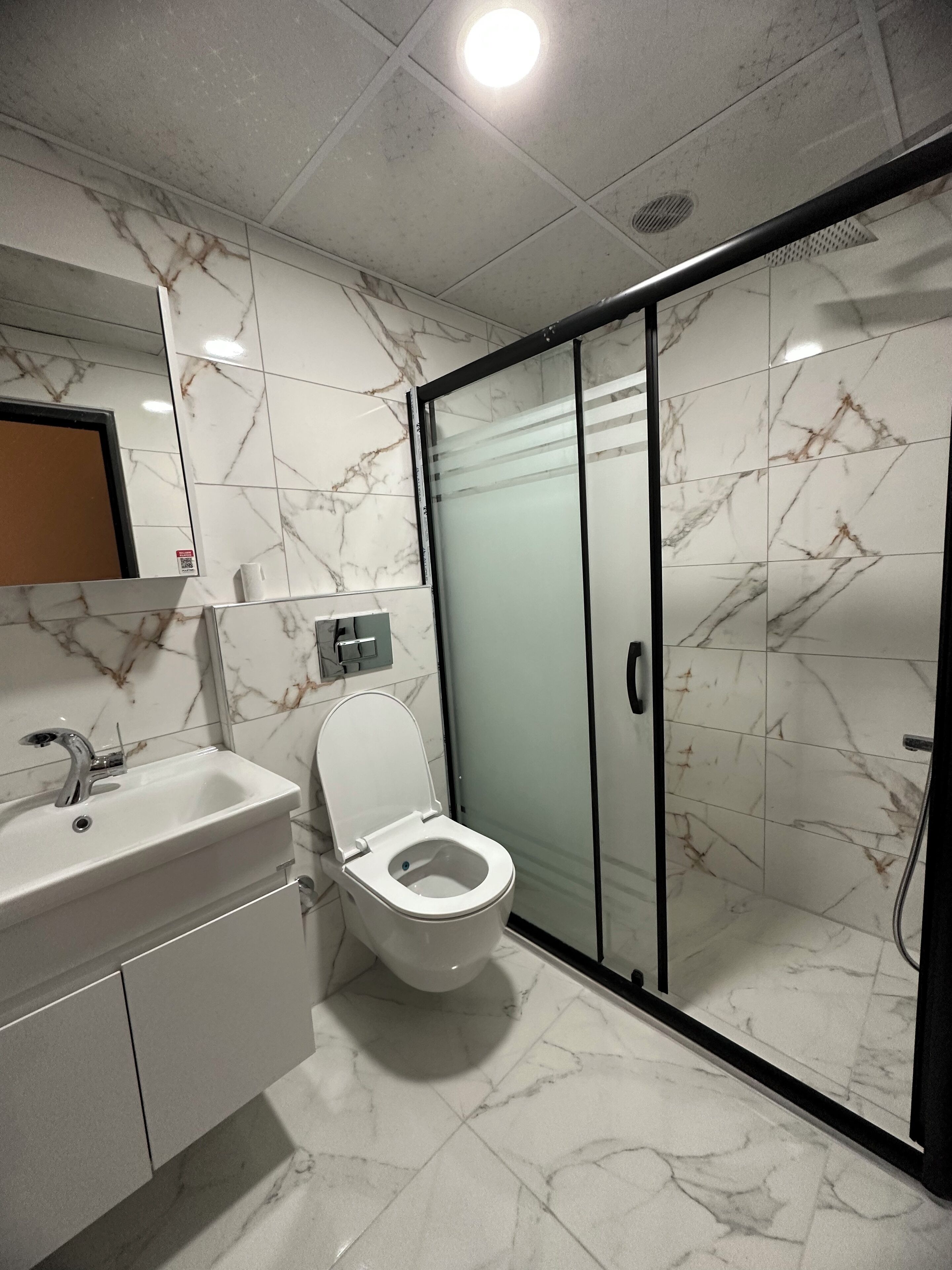 Une salle de bain moderne avec un sol en marbre, des toilettes blanches, un lavabo avec un miroir au-dessus et une cabine de douche en verre.