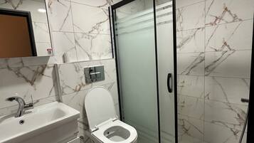 Une salle de bain moderne avec un sol en marbre, des toilettes blanches, un lavabo avec un miroir au-dessus et une cabine de douche en verre.