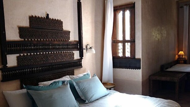 Une chambre à coucher avec un grand lit, de nombreux oreillers, une tête de lit en bois, une petite table et une fenêtre avec des rideaux.