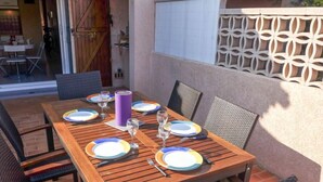 An outdoor dining area with a wooden table set for six, surrounded by wicker chairs. - Hameau des Tamarins by Interhome (Le Barcarès)