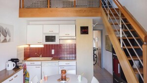 A modern kitchen with white cabinets, a red backsplash, a clock, and a wooden staircase. - Hameau des Tamarins by Interhome (Le Barcarès)