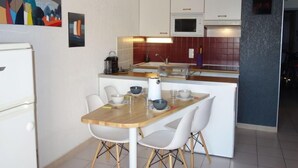 A modern kitchen with white cabinets, a microwave, and a coffee maker on the counter. There is a dining table with four chairs and a small island with a kettle and cups. - Hameau des Tamarins by Interhome (Le Barcarès)