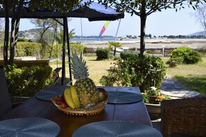 A table with a fruit bowl, outdoor seating, and a view of a beach and mountains.