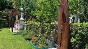 Una estructura de madera con un banco, rodeada por un jardín con diversas plantas y flores.