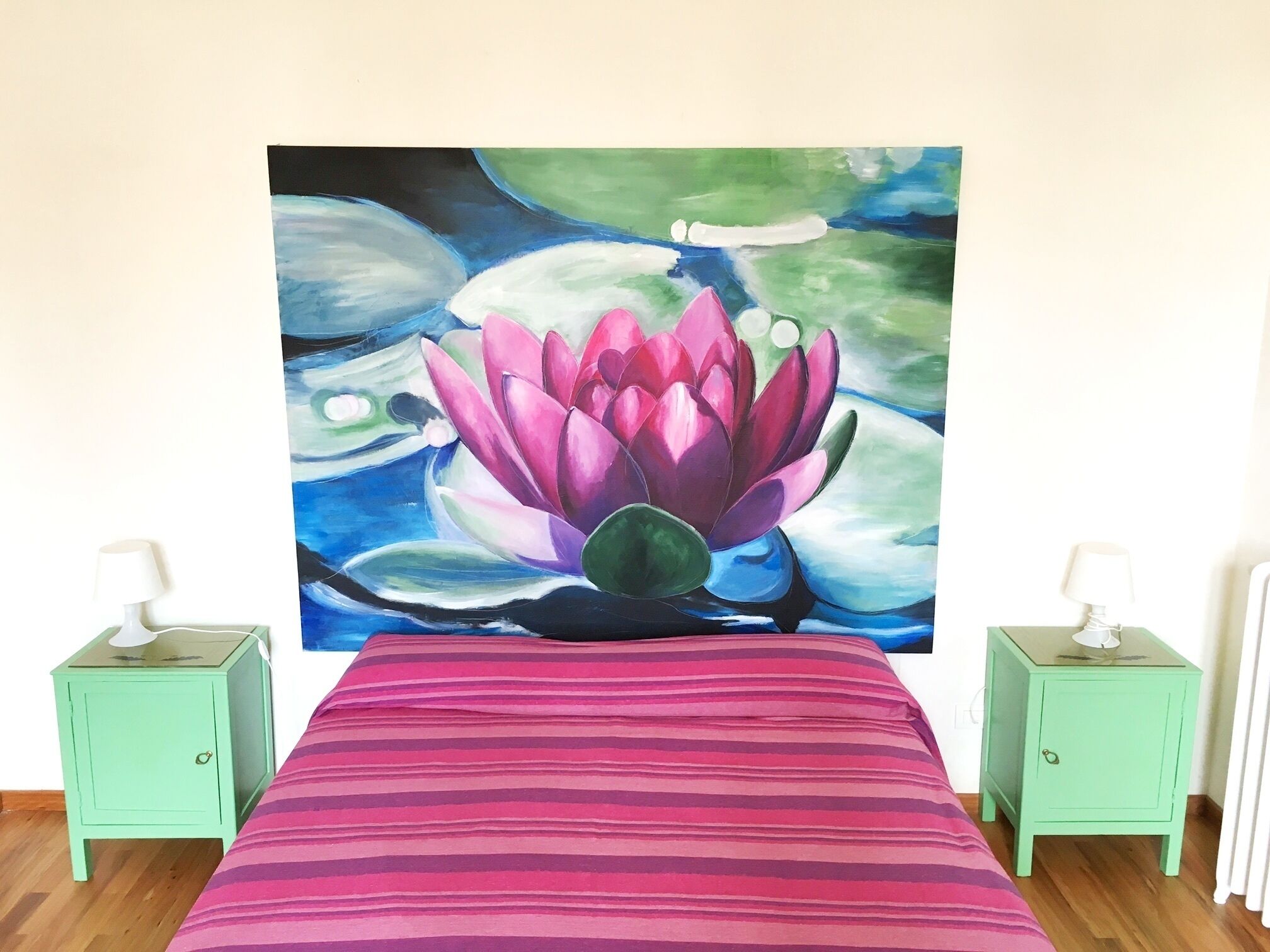 Una cama con una colcha a rayas, dos mesitas de noche con lámparas, y un cuadro grande de una flor de loto en la pared.