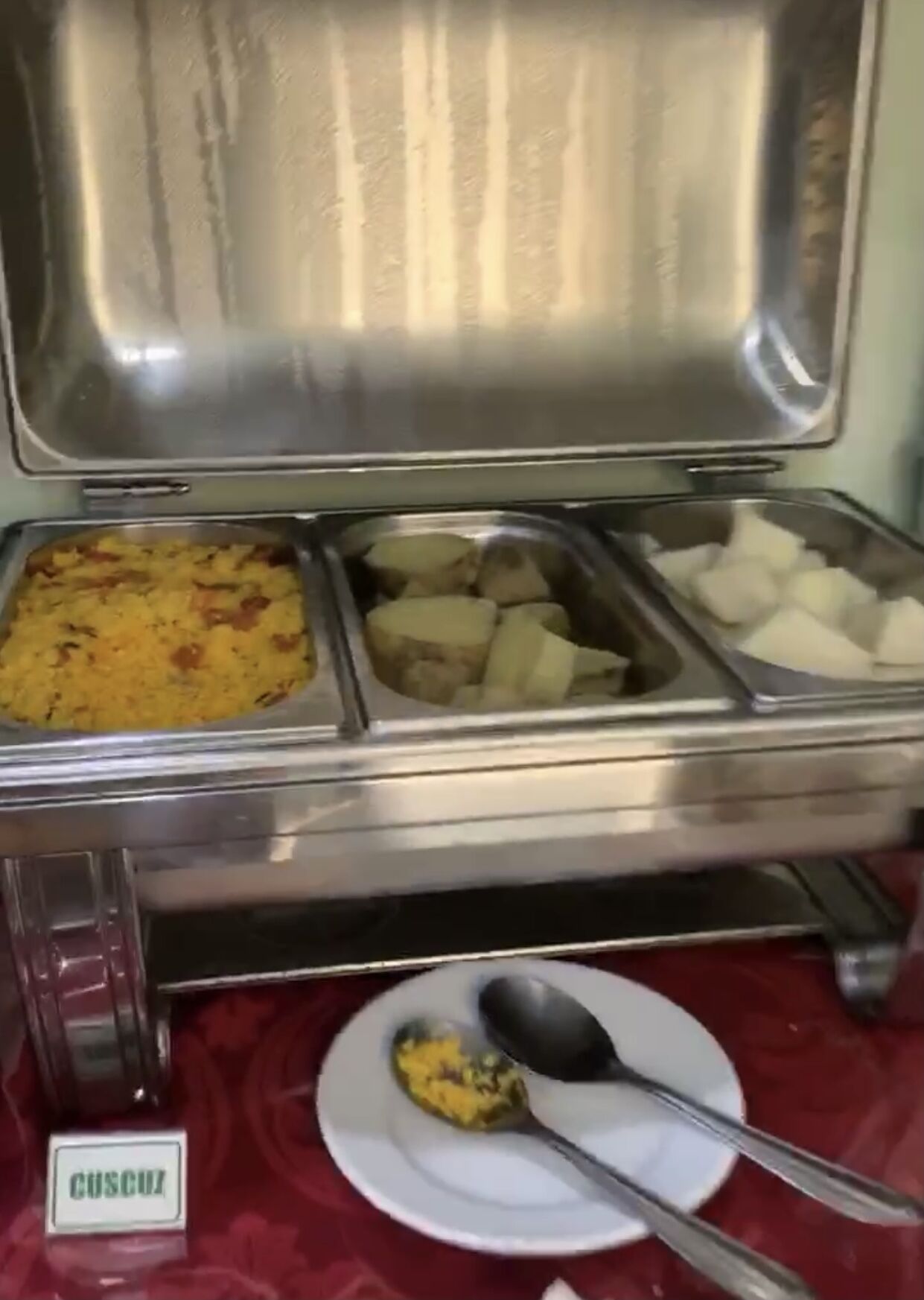 A buffet with various food items including rice, potatoes, and a dish labeled 'CUSCUZ'.