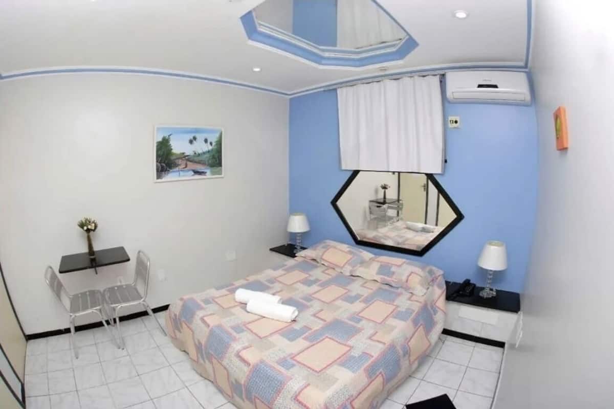 A bedroom with a bed, a desk, a chair, a mirror, and a picture on the wall.