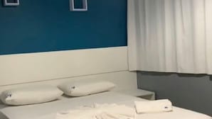 A hotel room with a bed, white pillows, a white duvet, a ceiling fan, and a window with white curtains. - Pousada Ferreira (Aracaju)
