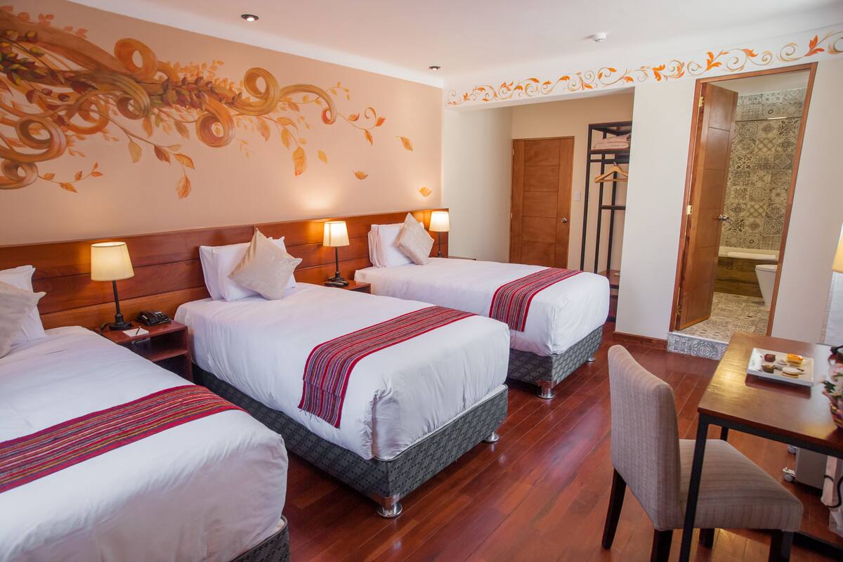 A hotel room with three beds, wooden headboards, and a dining table with a chair.