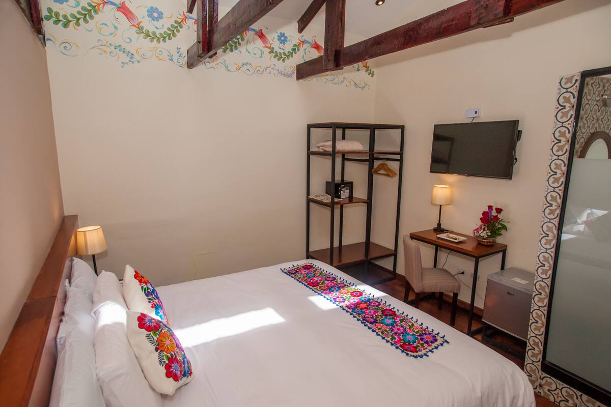 A hotel room with a bed, a desk, a chair, a TV, and a small cabinet.