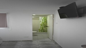 Un pasillo con un inodoro, una ducha con cortina de bambú y un televisor montado.