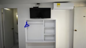 Una habitación con pared blanca, televisor montado y estante blanco con un perchero azul.