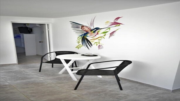 Un comedor con una mesa blanca y dos sillas negras, un mural colorido en la pared y un piso de baldosas.
