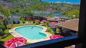 Una piscina con diseño en forma de corazón, rodeada de sillones de descanso y sombrillas, con vista a una zona residencial en la ladera.